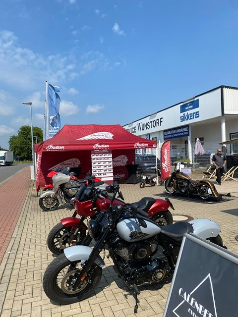 Drei Motorräder stehen vor einem roten Pavillon und einem Geschäft unter blauem Himmel