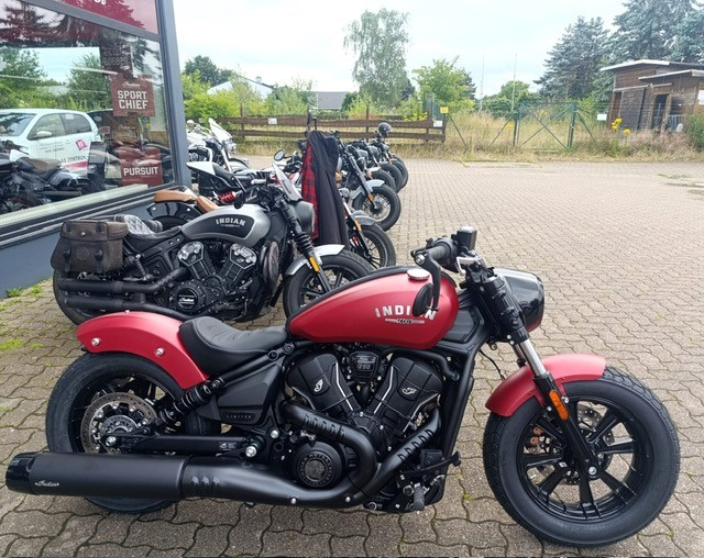 Ein rotes Motorrad steht auf einem Parkplatz mit weiteren Motorrädern im Hintergrund