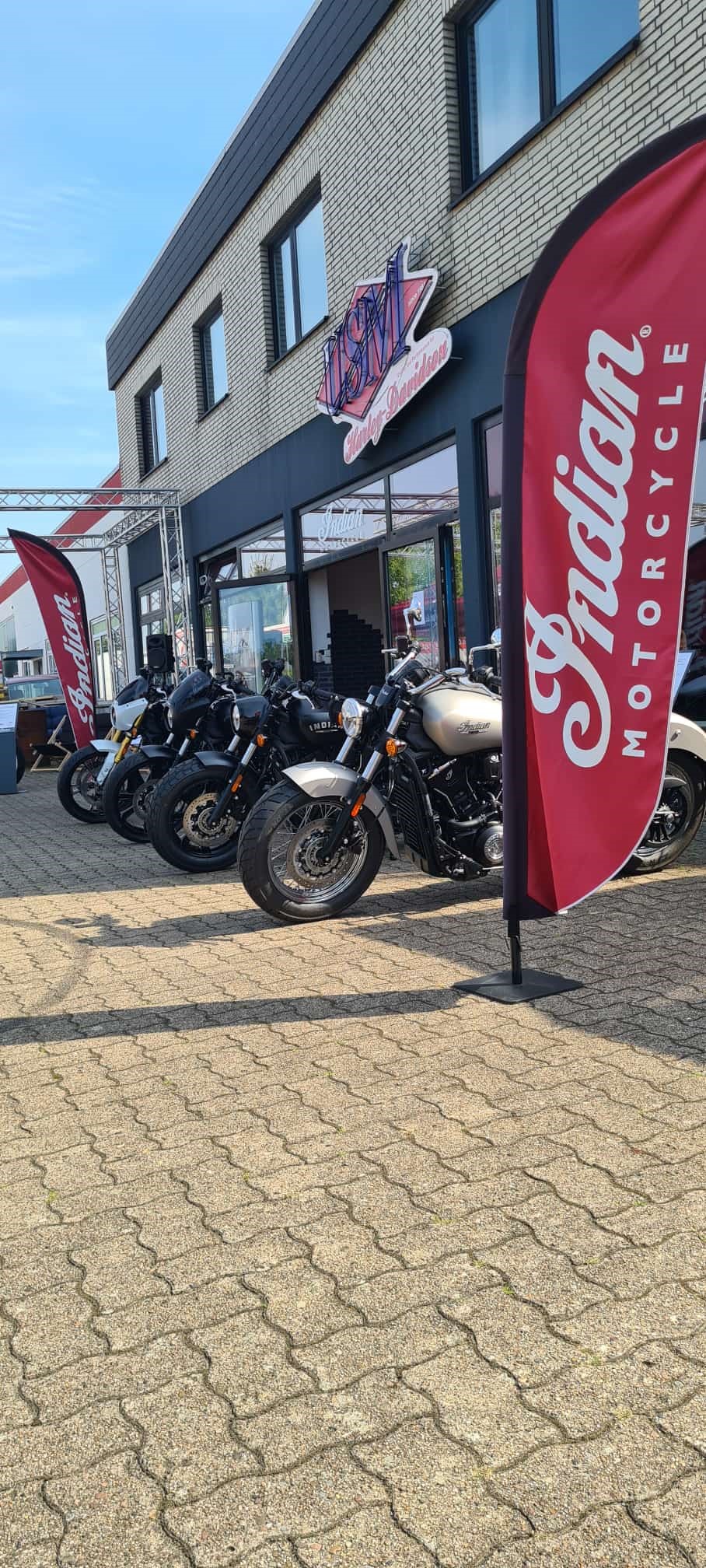 Mehrere schwarze Motorräder stehen vor einem modernen Gebäude mit roten Fahnen
