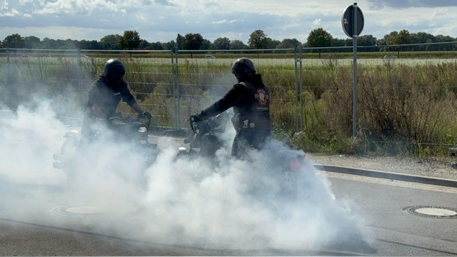 Zwei Motorradfahrer mit dunkler Kleidung machen Burnouts auf einer Straße mit viel Rauch