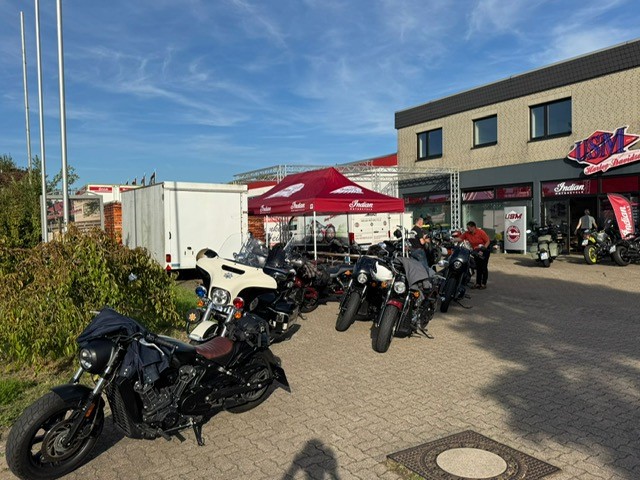 Mehrere Personen stehen lächelnd neben schwarzen Motorrädern vor einem Geschäft