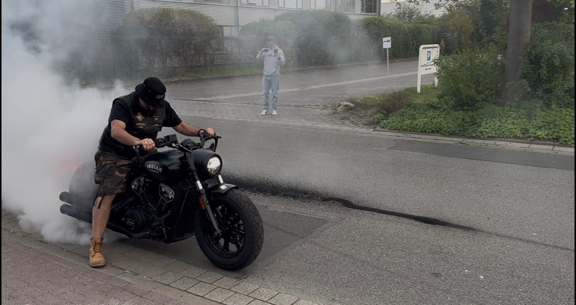 Ein Mann mit schwarzem Helm und Shirt macht auf einem schwarzen Motorrad Burnout