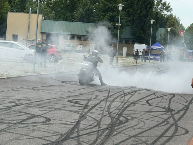 Eine Person mit Helm fährt rauchend einen grauen Motorrad und macht eine beeindruckende Drift auf einer mit vielen Reifenspuren bedeckten Straße