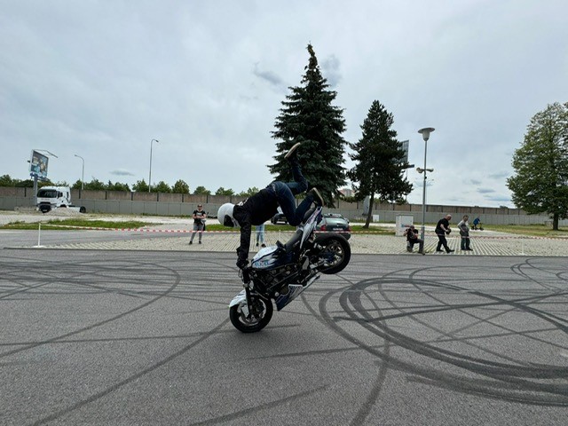 Eine Person mit schwarzer Kleidung macht einen Stunt auf einem Motorrad und wirkt konzentriert
