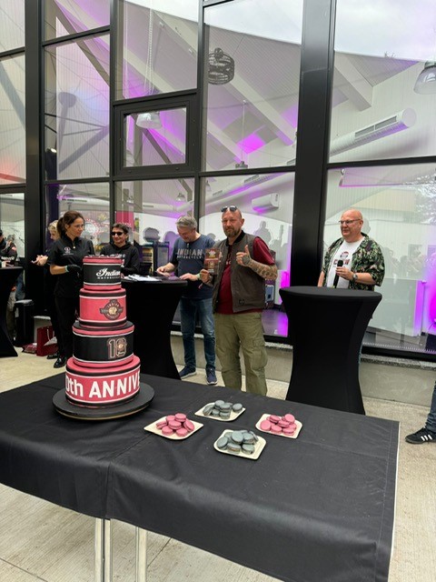 Ein bärtiger Mann mit rotem Hemd lächelt neben einer großen mehrstöckigen Torte